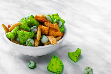 Japanese hot snacks with peanuts and wasabi lie in a white bowl and on a white marble surface