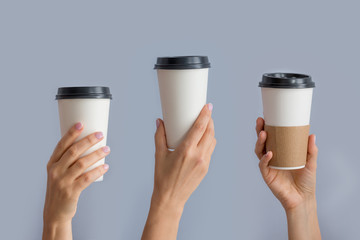 Mockup of several female hands holding up a Coffee paper cup isolated on grey background. Front view