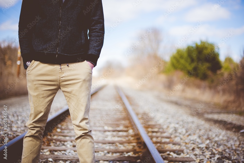 Wall mural Closeup shot of a male standing on train tracks while his hands in the pocket