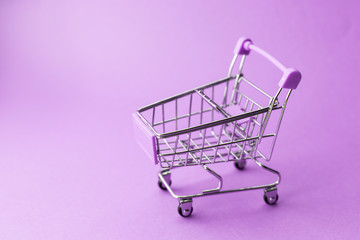 empty metal shopping trolley on purple background. Discount and shopping concept