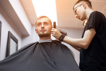Uzbek hairdresser cuts a young handsome guy in a barbershop, a male client sits in a beauty salon and makes a short haircut
