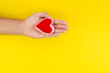 Romantic Valentine's day card concept with Person's hand holding a handmade red felt heart on clear yellow background. Top view mockup with copy space for text
