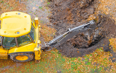 Yellow tractor excavator digs a pit with a bucket, accident. Breakthrough underground. Autumn...