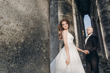Gorgeous wedding couple embracing in sunlight near old castle in beautiful park. Stylish beautiful...