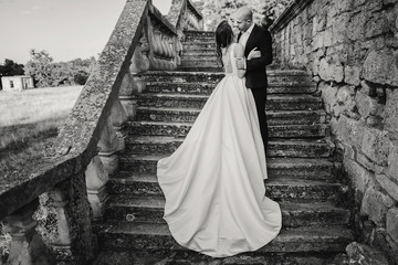 Gorgeous wedding couple embracing on stone stairs near old castle in park. Stylish beautiful bride...