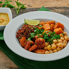 Buddha nourish bowl with garlic grilled shrimps, baked sweet potato, black quinoa, chickpeas, humus and lime on a table.