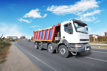 Dump truck in motion on the countryside road against blue sky with clouds