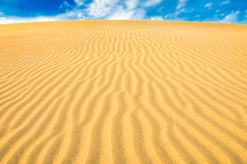 Landscape of desert sand dunes and blue sky with clouds over them