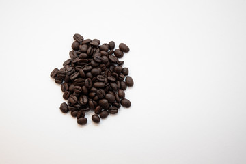 Dark roasted coffee beans on a pile on a white surface