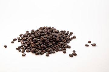 Dark roasted coffee beans on a pile on a white surface