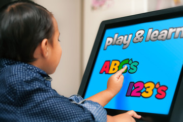 A little kid looking at a touchscreen and using his index finger to learn his ABC's and numbers.