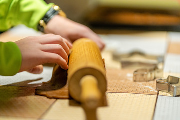 Kid in green jacket rolling dough for gingerbread cookies