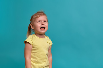 Close-up studio shot of a beautiful little girl. Little blonde girl in a yellow T-shirt on a blue background. The emotions of a child.