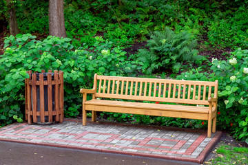wooden bench with a wooden trash can in the park with green plants on a summer day, nobody.