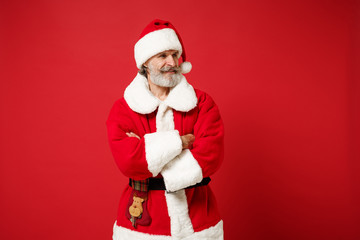 Smiling elderly gray-haired mustache bearded Santa man in Christmas hat posing isolated on red background. Happy New Year 2020 celebration holiday concept. Mock up copy space. Holding hands crossed.