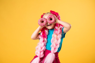 little girl with donuts on yellow background isolate, space for text