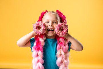 little girl with donuts on yellow background isolate, space for text