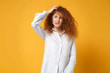 Preoccupied young redhead woman girl in casual white shirt posing isolated on yellow orange background studio portrait. People lifestyle concept. Mock up copy space. Putting hand on head, biting lips.