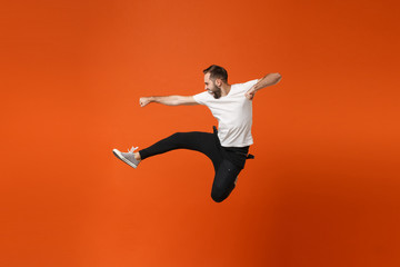 Crazy young man in casual white t-shirt posing isolated on orange wall background studio portrait. People lifestyle concept. Mock up copy space. Having fun jumping, fooling around, clenching fists.