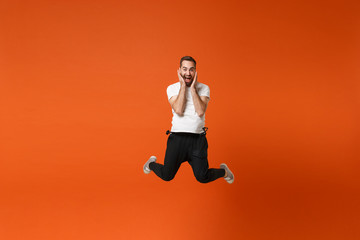 Fototapeta na wymiar Excited funny young man in casual white t-shirt posing isolated on bright orange wall background studio portrait. People lifestyle concept. Mock up copy space. Having fun, fooling around, jumping.