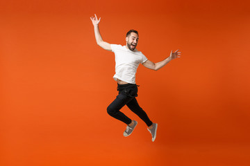 Fototapeta na wymiar Cheerful young man in casual white t-shirt posing isolated on orange wall background studio portrait. People lifestyle concept. Mock up copy space. Having fun, fooling around, jumping spreading hands.