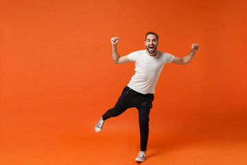 Fototapeta na wymiar Cheerful young man in casual white t-shirt posing isolated on bright orange wall background studio portrait. People sincere emotions lifestyle concept. Mock up copy space. Clenching fists like winner.