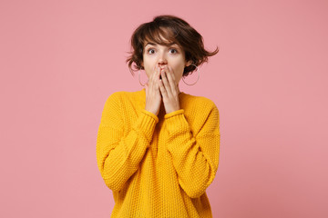 Shocked young brunette woman girl in yellow sweater posing isolated on pastel pink background studio portrait. People sincere emotions lifestyle concept. Mock up copy space. Covering mouth with hands.
