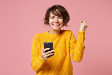 Joyful young brunette woman girl in yellow sweater posing isolated on pastel pink background....