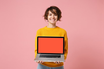 Naklejka premium Smiling young brunette woman girl in yellow sweater posing isolated on pink wall background in studio. People lifestyle concept. Mock up copy space. Holding laptop pc computer with blank empty screen.