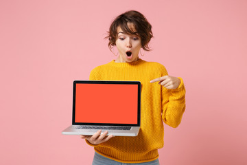 Shocked young brunette woman girl in yellow sweater posing isolated on pink background. People lifestyle concept. Mock up copy space. Point index finger on laptop pc computer with blank empty screen.