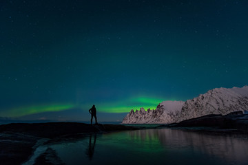 Man watching the northern lights, Aurora Borealis, Devil Teeth mountains in the background, Tungeneset, Senja, Norway
