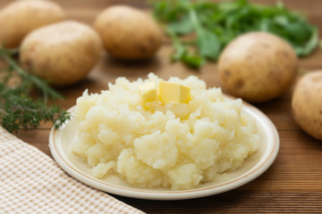 Mashed potatoes with butter and fresh white potatoes on background, wooden table. Healthy food for kids, dinner.