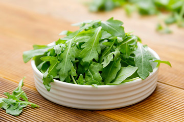 Fresh green rocket salad in white round plate. Healthy salad isolated on wooden table. Copy space.