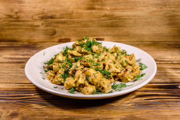Plate with champignons stewed in sour cream on a wooden table