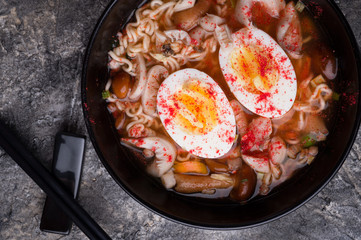spicy instant noodles soup with shrimps, egg and  mushrooms. served  by black chopsticks. flat lay. close up