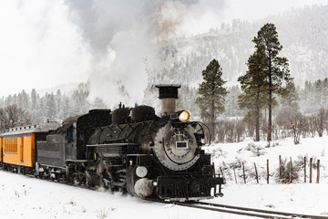 Plakaty  Vintage parowy pociąg kłębiący się dym w śniegu, gdy porusza się po górach.