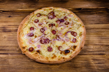 Pizza with sausages, ham and parmesan cheese on a wooden table