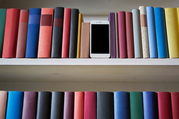 Low angle of colorful bookshelf with mobile phone between books