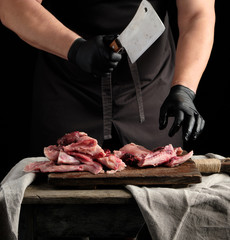 chef in black latex gloves holds a big knife and cuts into pieces raw rabbit meat
