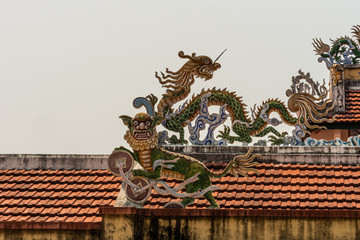 Nha Trang, Vietnam - March 11, 2019: Dinh Phu Vinh community center and celebration hall. Closeup on corner piece of Dragon statues as decorations on red roof against silver sky .