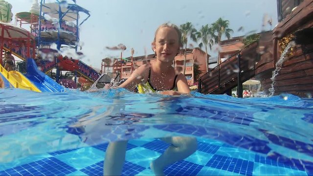 Happy girl playing in outdoor swimming pool on summer vacation on tropical beach.