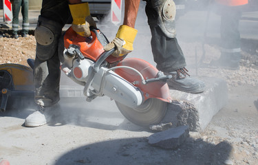 Builder worker with cut-off machine power tool breaking concrete at road construction site 
