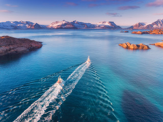 Aerial view of fishing boats, rocks in the blue sea, snowy mountains and colorful sky with clouds at sunset in winter in Lofoten islands, Norway, Landscape with two motorboats. Top view. Travel - obrazy, fototapety, plakaty
