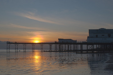 Fototapeta na wymiar Beautiful sunset behind and reflections on the sand at low tide behind the Pier in Bognor Regis West Sussex.