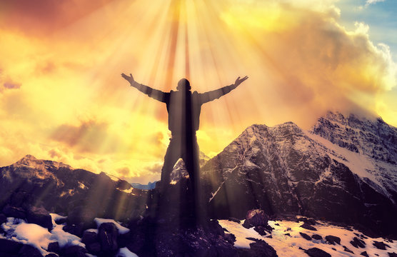 Man Praying With Arms Open On Epic Mountain Top Summit With Light Shining With Arms Out On Top Of Mountain Peak	