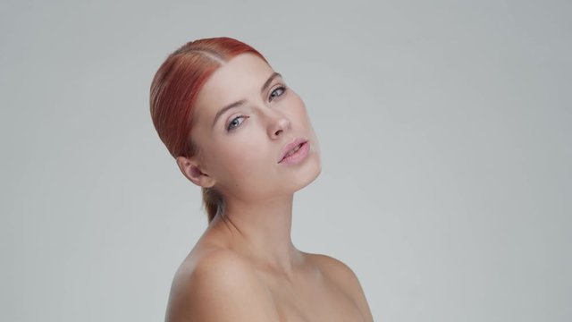 Studio portrait of young, beautiful and natural redhead woman applying skin care cream. Face lifting, cosmetics and make-up.