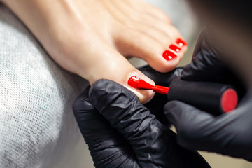 Woman receiving nail polishing with red nail polish on fingers of feet by professional podiatrist...