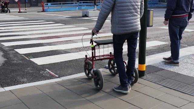 disabled person with a walker crosses the road at a pedestrian crossing