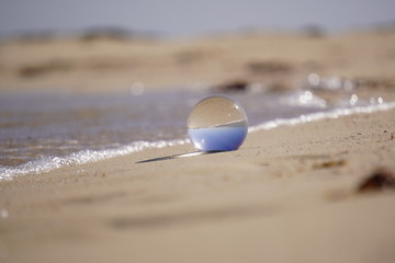 Fototapeta na wymiar Crystal lens ball with waves and sandy beach
