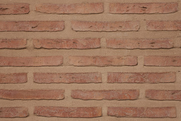 An old wall is constructed of orange red clay bricks showing a rustic and worn texture.